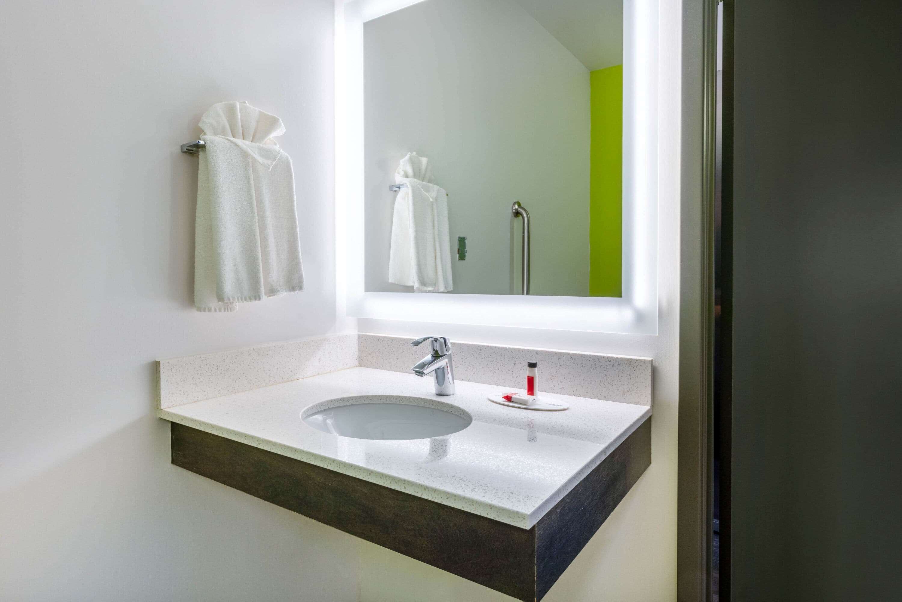 Ein modernes Badezimmer mit einem weißen Waschbecken, einem Spiegel und zwei Handtüchern, die an der Wand hängen.