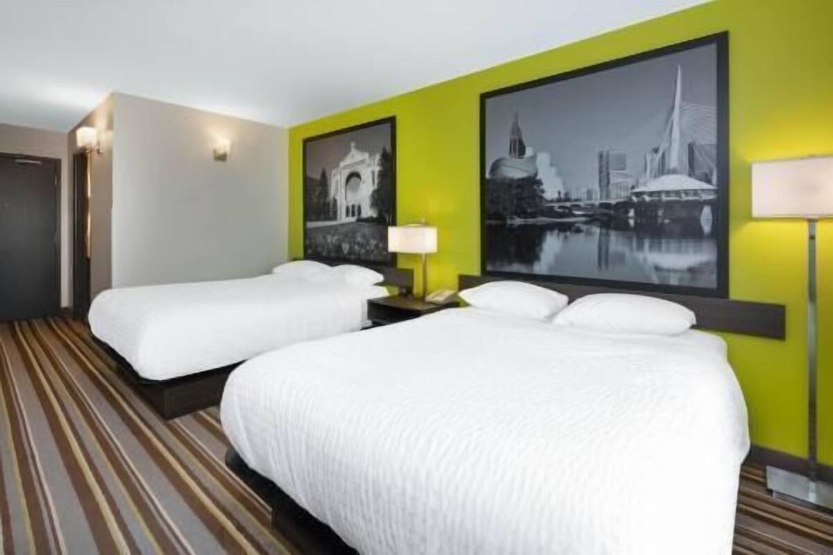 Una habitación de hotel con dos camas, una alfombra a rayas y dos lámparas fijadas a la pared.