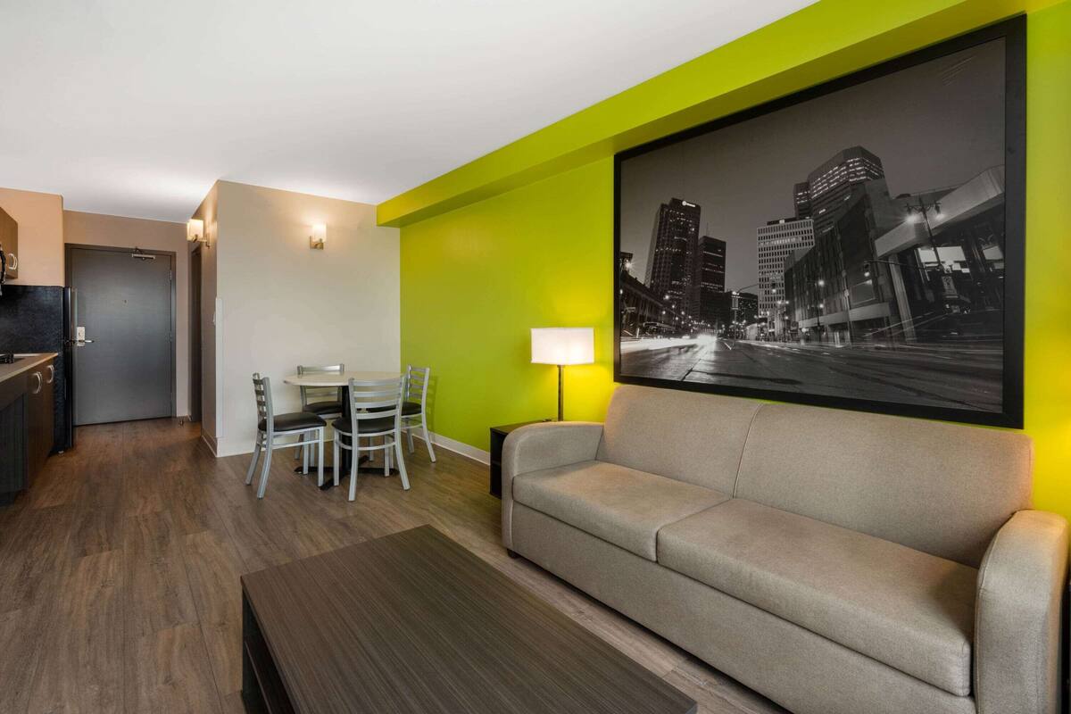 Una habitación de hotel moderna con comedor, sofá y un cuadro de un paisaje urbano.