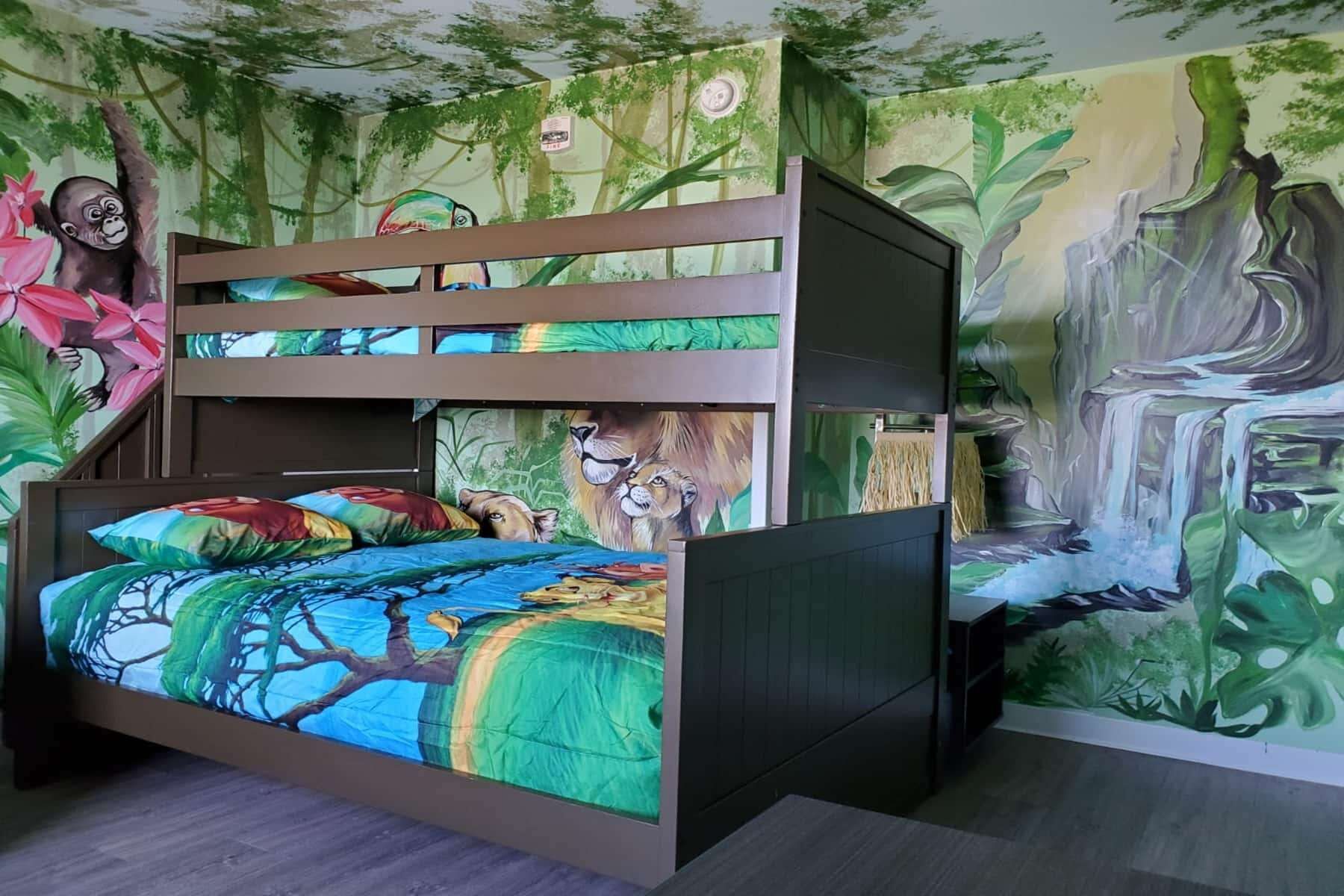 A bunk bed with a jungle-themed mural on the walls, a television, and a small table.