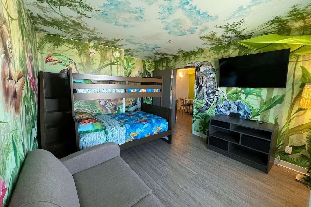 Una habitación con literas, un televisor de pantalla plana y un mural con una escena selvática.