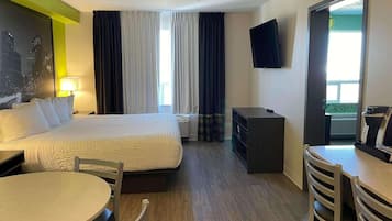 Habitación de hotel con cama, escritorio, silla, mesa, televisor y ventana con cortinas.