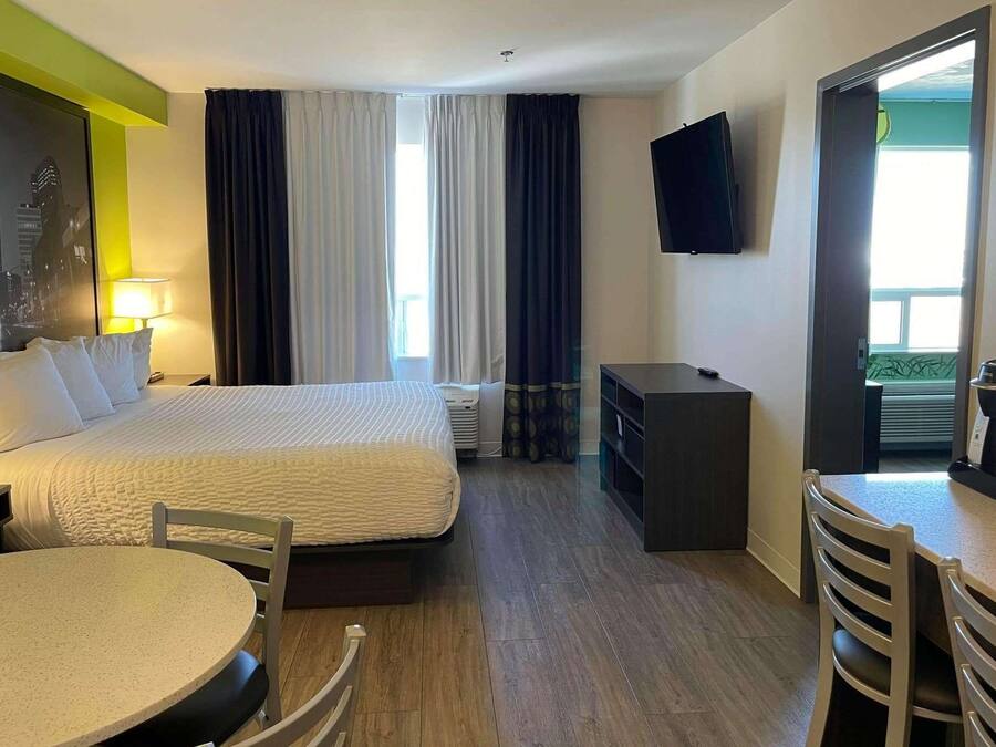 Habitación de hotel con cama, escritorio, silla, mesa, televisor y ventana con cortinas.