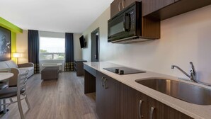 A modern kitchen with a microwave, sink, and cabinets. There is a dining area with a table and chairs, and a view of the outdoors through a window. - Super 8 by Wyndham Winnipeg East MB (Winnipeg)