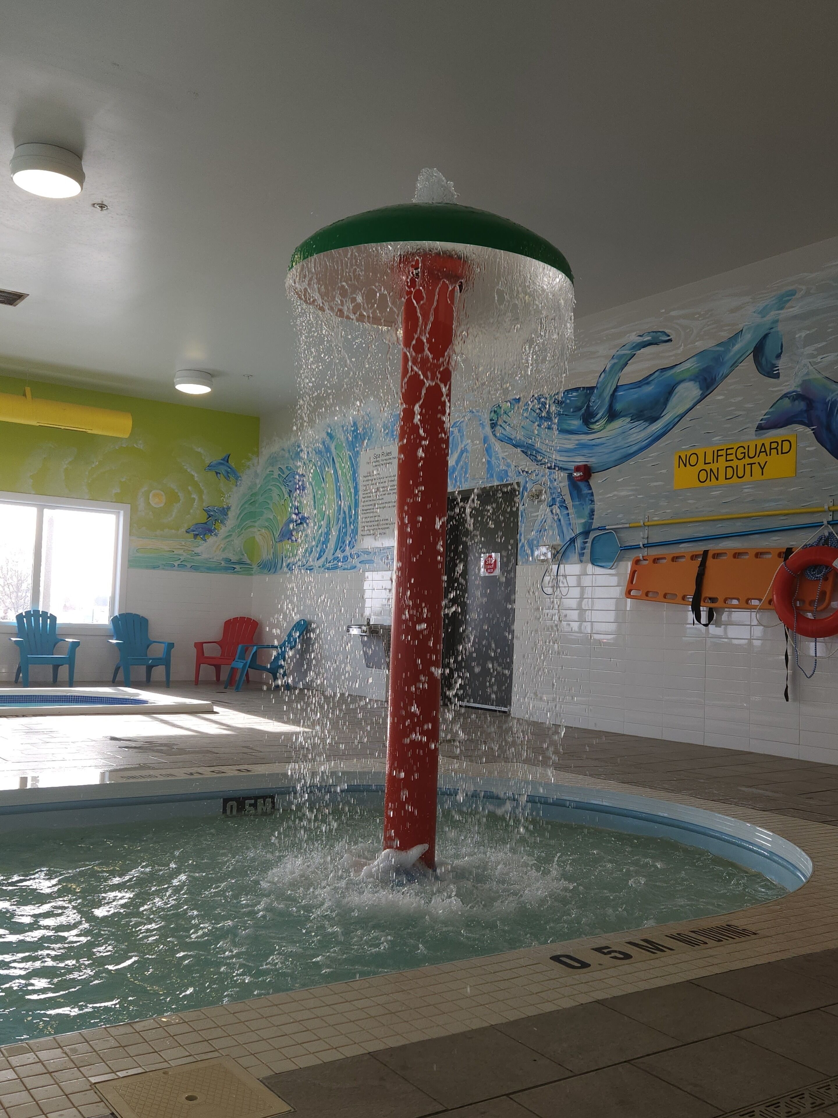 Una piscina interior con una fuente de agua, un letrero de salvavidas y coloridos murales en las paredes.