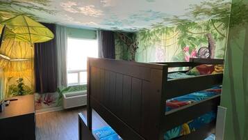 Una habitación con literas, un escritorio, una lámpara y un mural con un paisaje forestal.