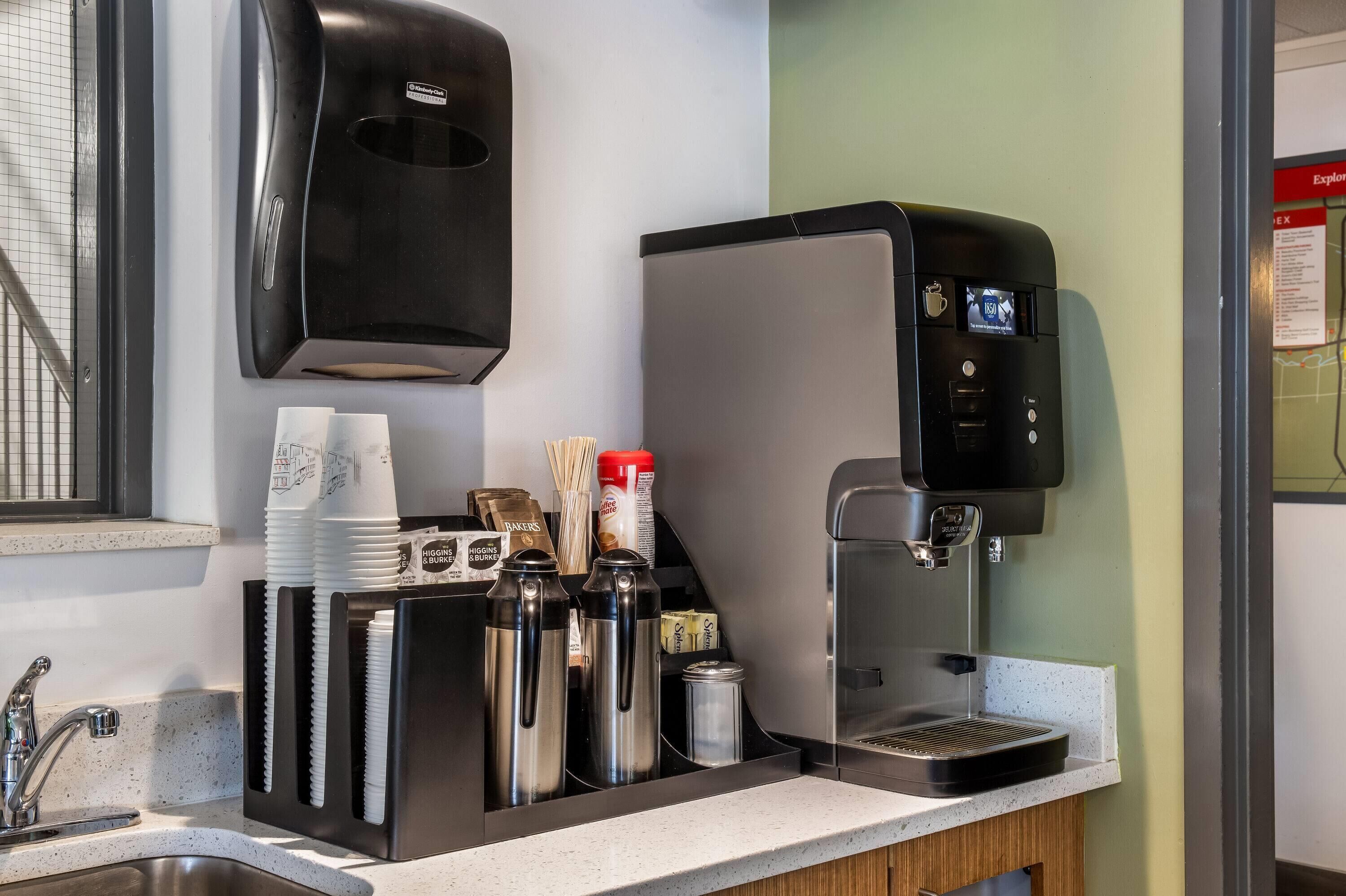Una màquina de cafè, un dispensador de tovallons de paper i un suport per a tasses amb diversos objectes.