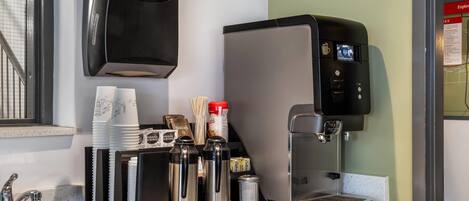 Una màquina de cafè, un dispensador de tovallons de paper i un suport per a tasses amb diversos objectes.