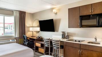 A hotel room with a bed, desk, chairs, a TV, a microwave, and a sink.