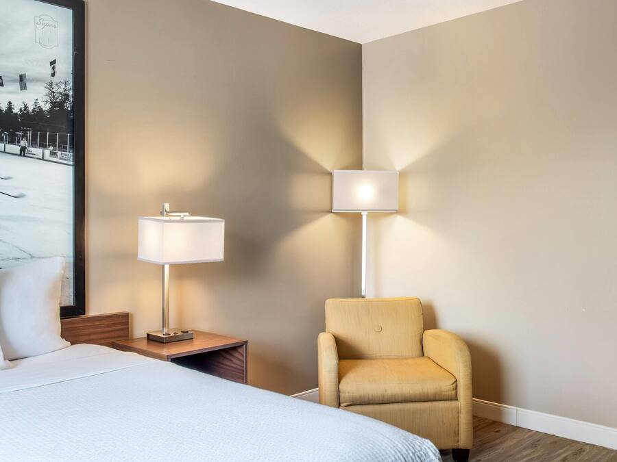 Ett hotellrum med en säng, ett nattduksbord, en lampa, en stol och en väggmonterad lampa.