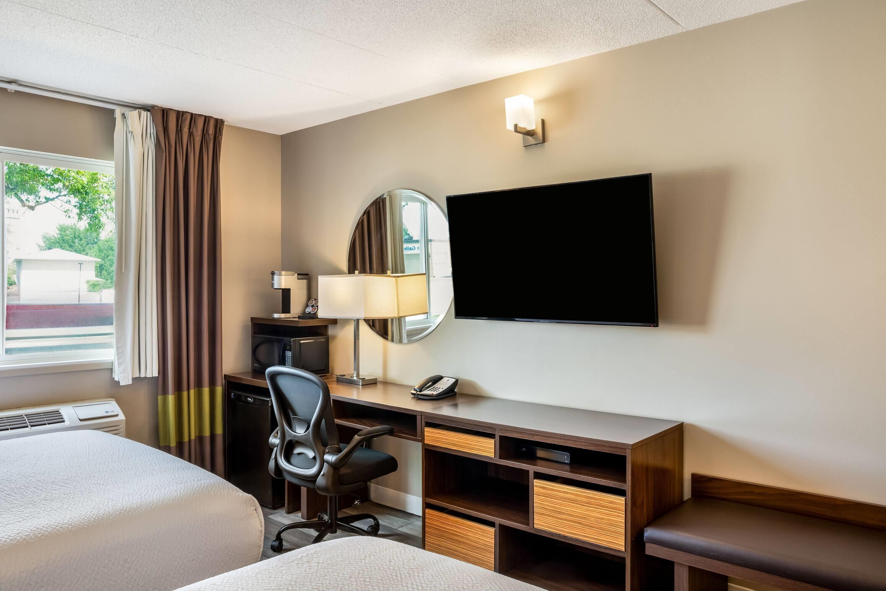 A hotel room with a bed, desk, chair, TV, lamp, and a window with curtains.
