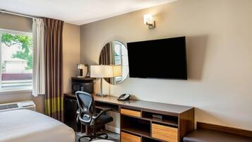 A hotel room with a bed, desk, chair, TV, lamp, and a window with curtains.