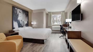 Habitación de hotel con una cama grande, un escritorio, una silla, un banco, un televisor y una ventana con cortinas.