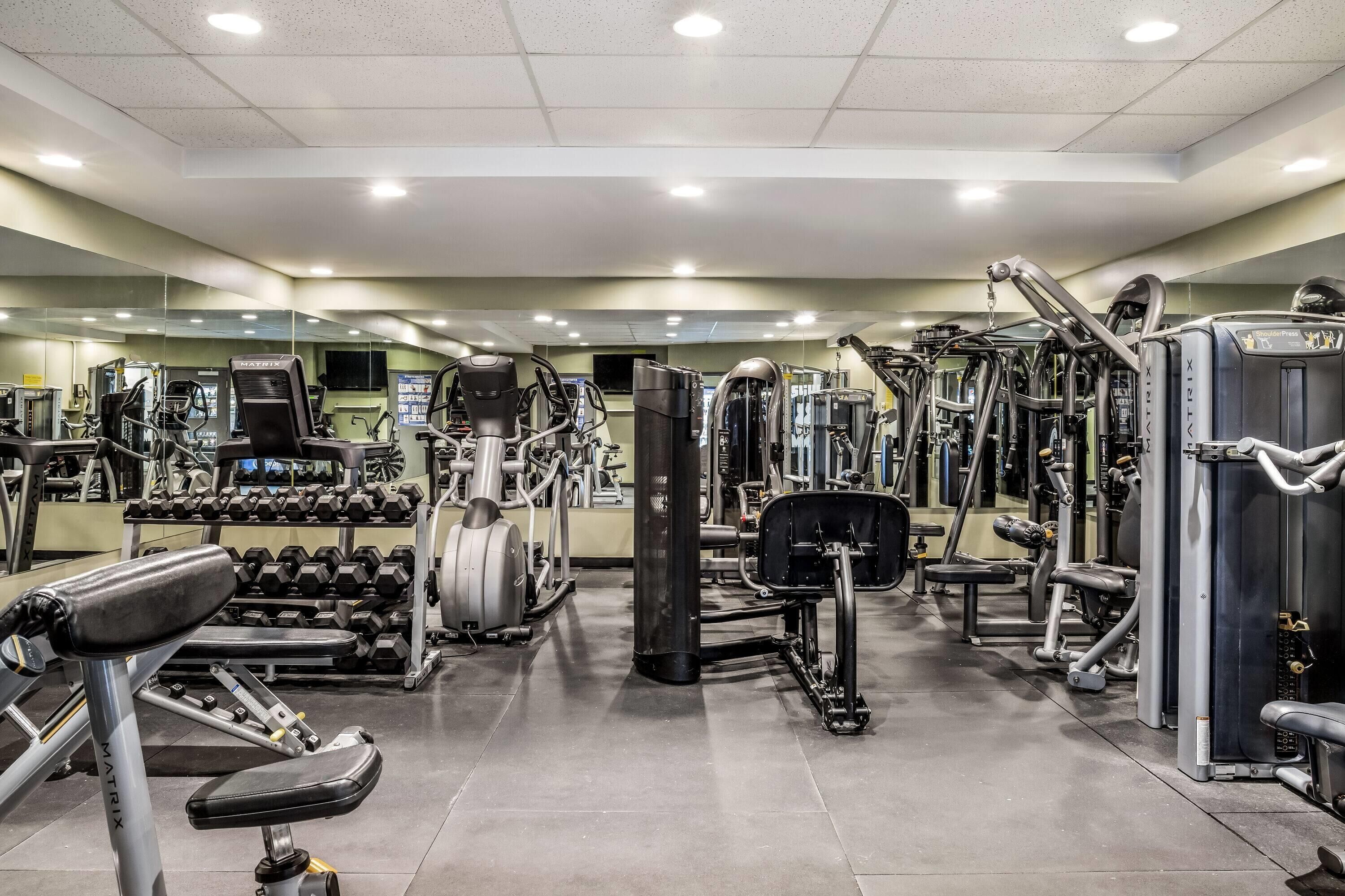 Un gimnasio con diferentes máquinas de ejercicio, estantes para pesas y espejos en las paredes.