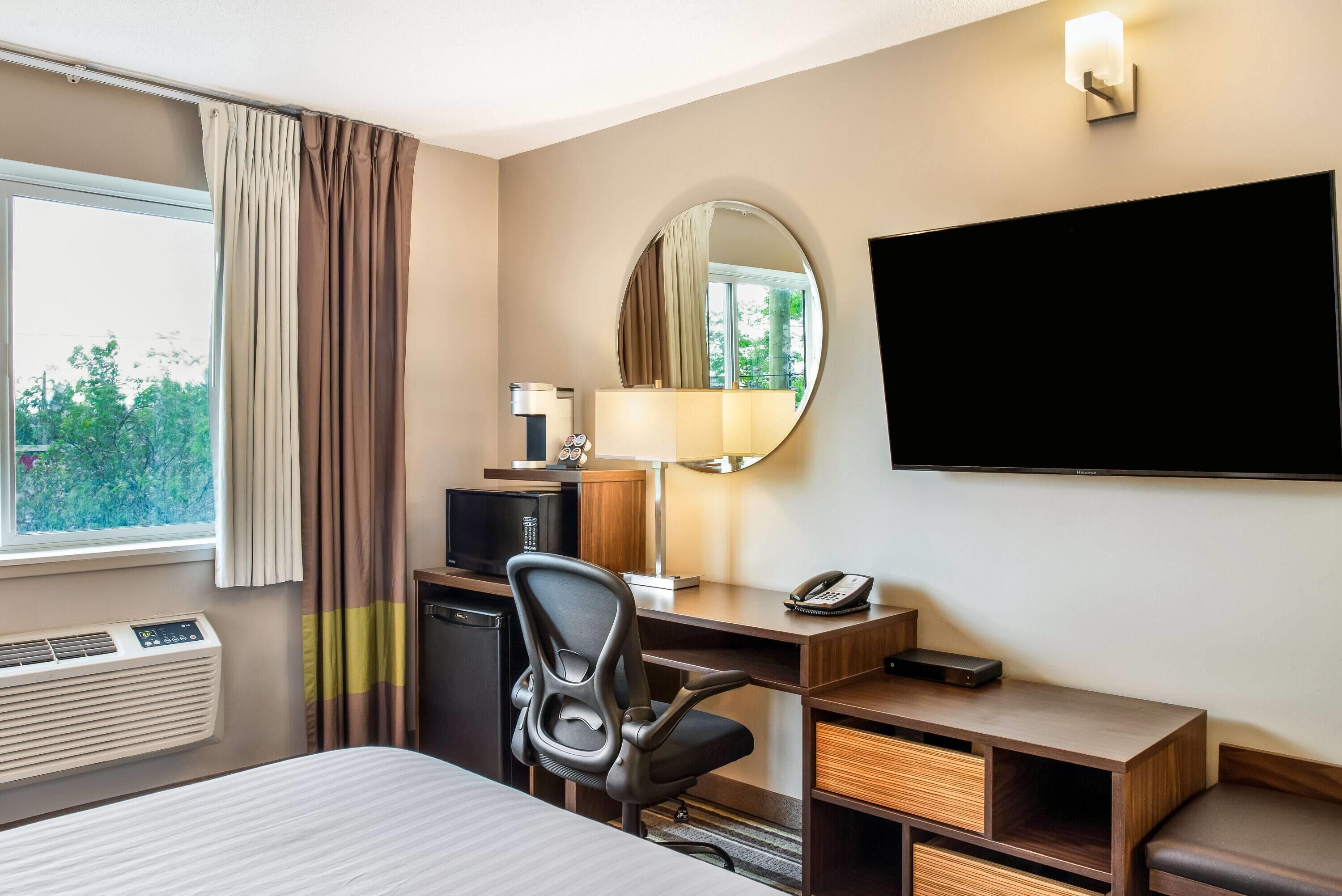 A hotel room with a bed, desk, chair, TV, and window with curtains.