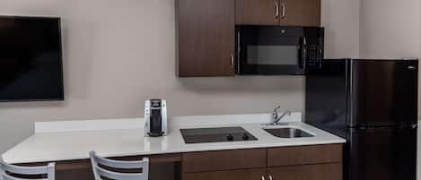 A compact kitchen with a microwave, refrigerator, and a coffee maker on the counter.