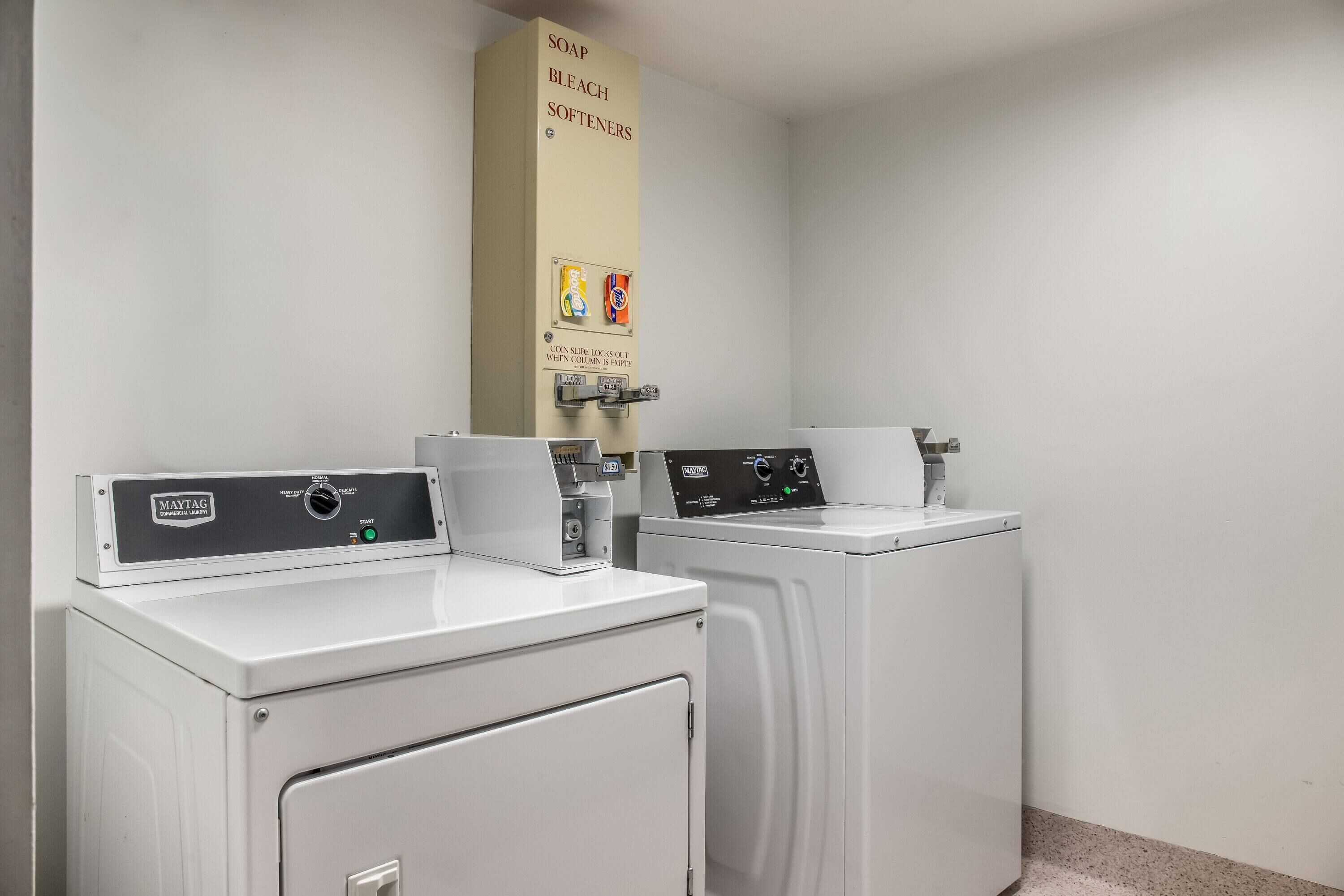A laundry facility with two front-loading washing machines and a soap, bleach, and softeners dispenser.
