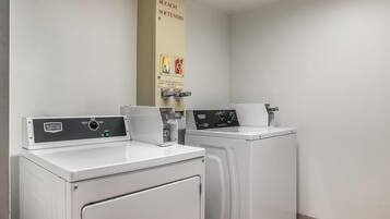 A laundry facility with two front-loading washing machines and a soap, bleach, and softeners dispenser.