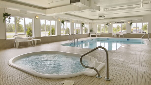 A large indoor swimming pool with a separate hot tub area, surrounded by windows and chairs.