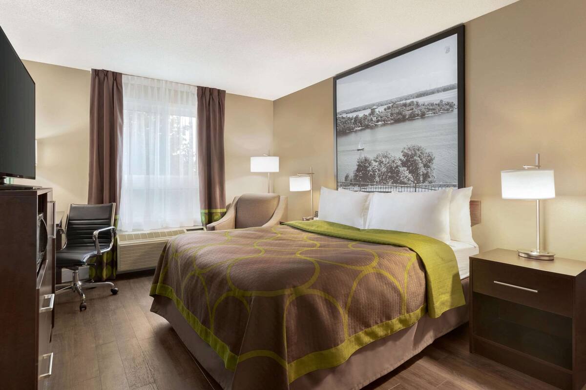 Ein Hotelzimmer mit einem großen Bett, einem Schreibtisch mit Stuhl, zwei Nachttischlampen und einem großen Fenster mit Blick auf ein Gewässer.