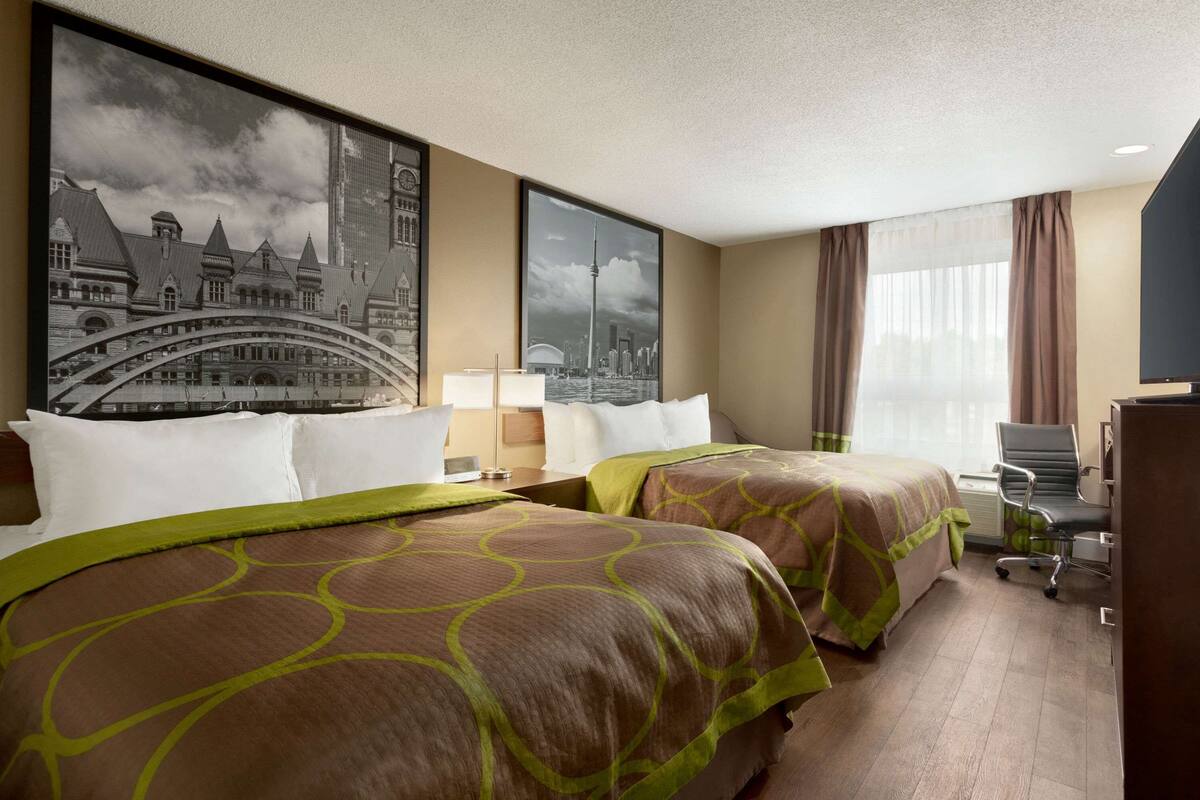 Ein Hotelzimmer mit zwei Betten, einem Schreibtisch, einem Stuhl und einem großen Fenster mit Vorhängen.