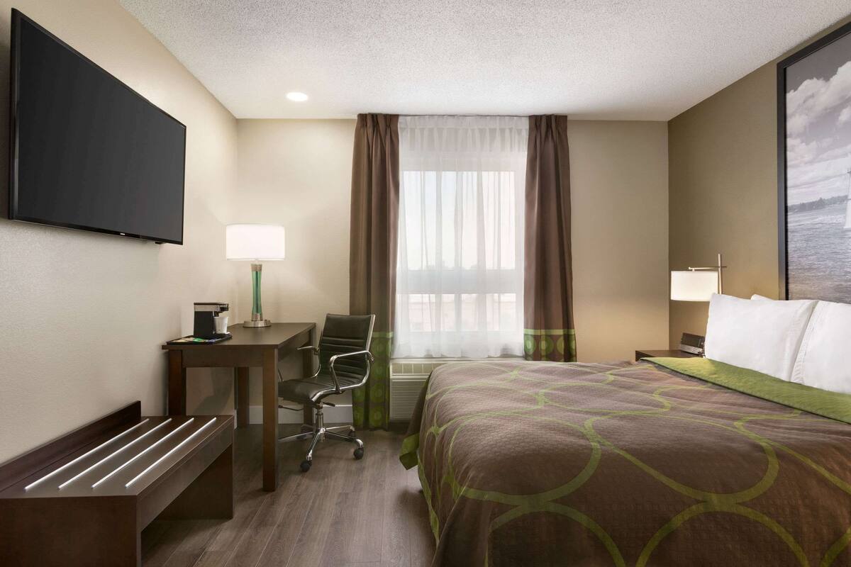 Ein Hotelzimmer mit Bett, Schreibtisch, Stuhl, Fernseher und einem Fenster mit Vorhängen.