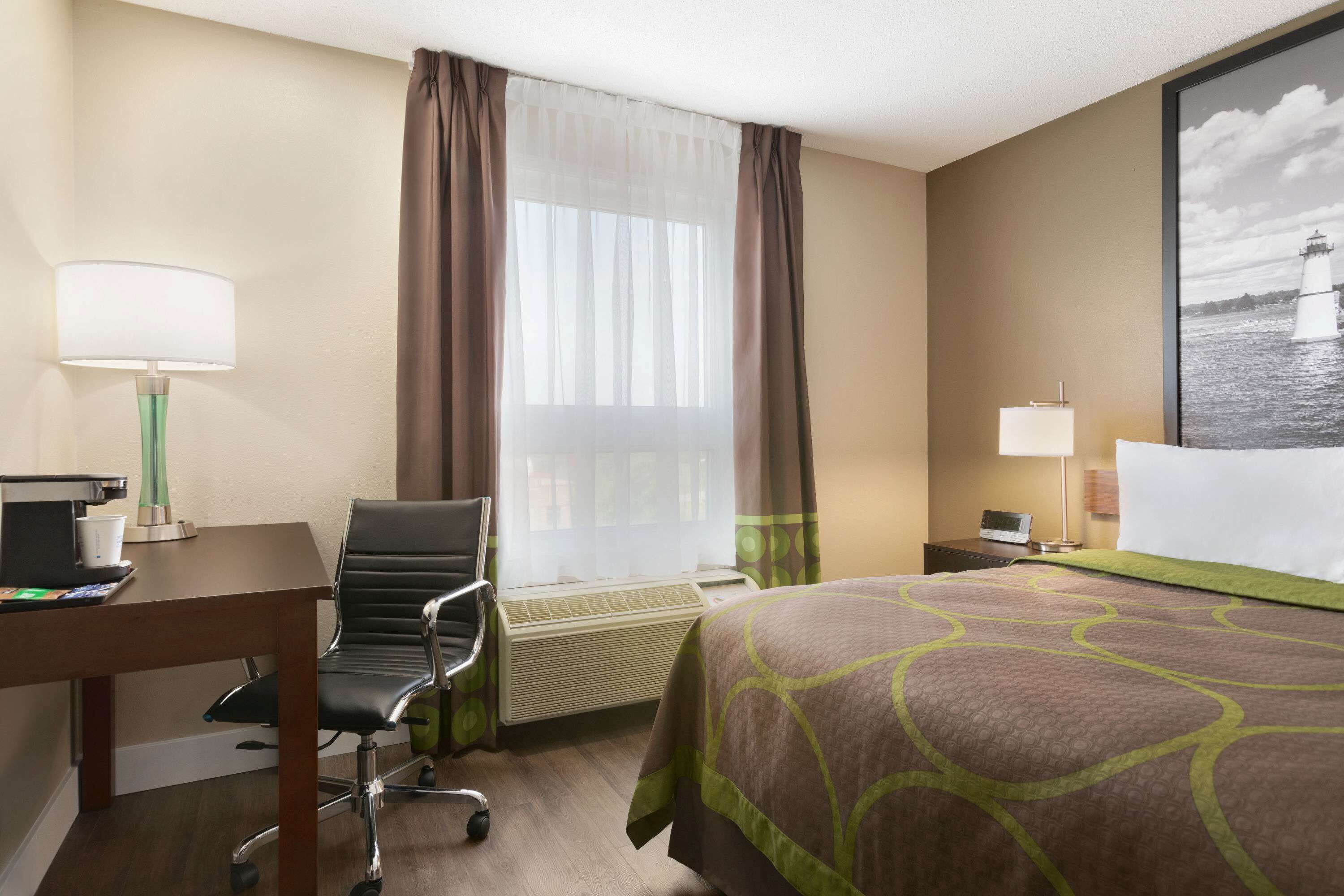 Ein Hotelzimmer mit Bett, Schreibtisch, Stuhl, Lampe, Klimaanlage und einem Fenster mit Vorhängen.