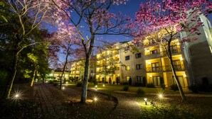 Un hôtel à plusieurs étages doté d’une cour intérieure, de chemins éclairés et de cerisiers en fleurs.
