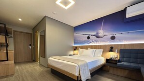 Une chambre d’hôtel moderne dotée d’un grand lit, de tables de chevet, d’un coin salon et d’une fresque représentant un avion peinte au plafond.