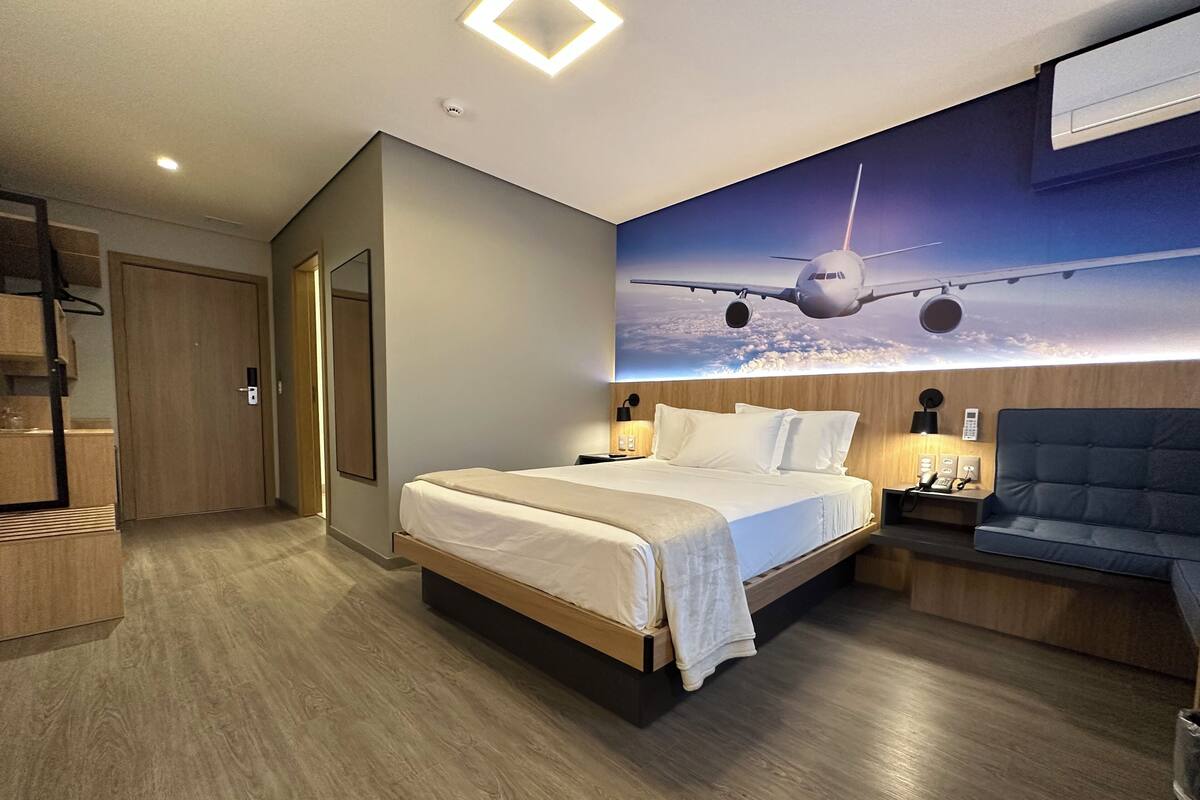 Une chambre d’hôtel moderne dotée d’un grand lit, de tables de chevet, d’un coin salon et d’une fresque représentant un avion peinte au plafond.