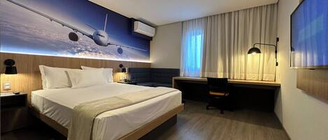 Une chambre d’hôtel moderne équipée d’un grand lit, d’un bureau, d’une chaise et d’un téléviseur fixé au mur.