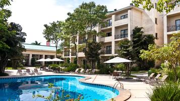 A swimming pool surrounded by lounge chairs and umbrellas, with a building in the background.