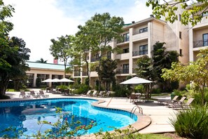 Una piscina rodeada de sillas de descanso y sombrillas, con un edificio al fondo.