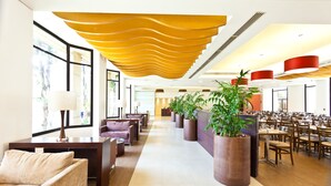 Un hall d’entrée spacieux au design moderne, comprenant un long comptoir d’accueil, des espaces de détente confortables et de grandes plantes en pot.