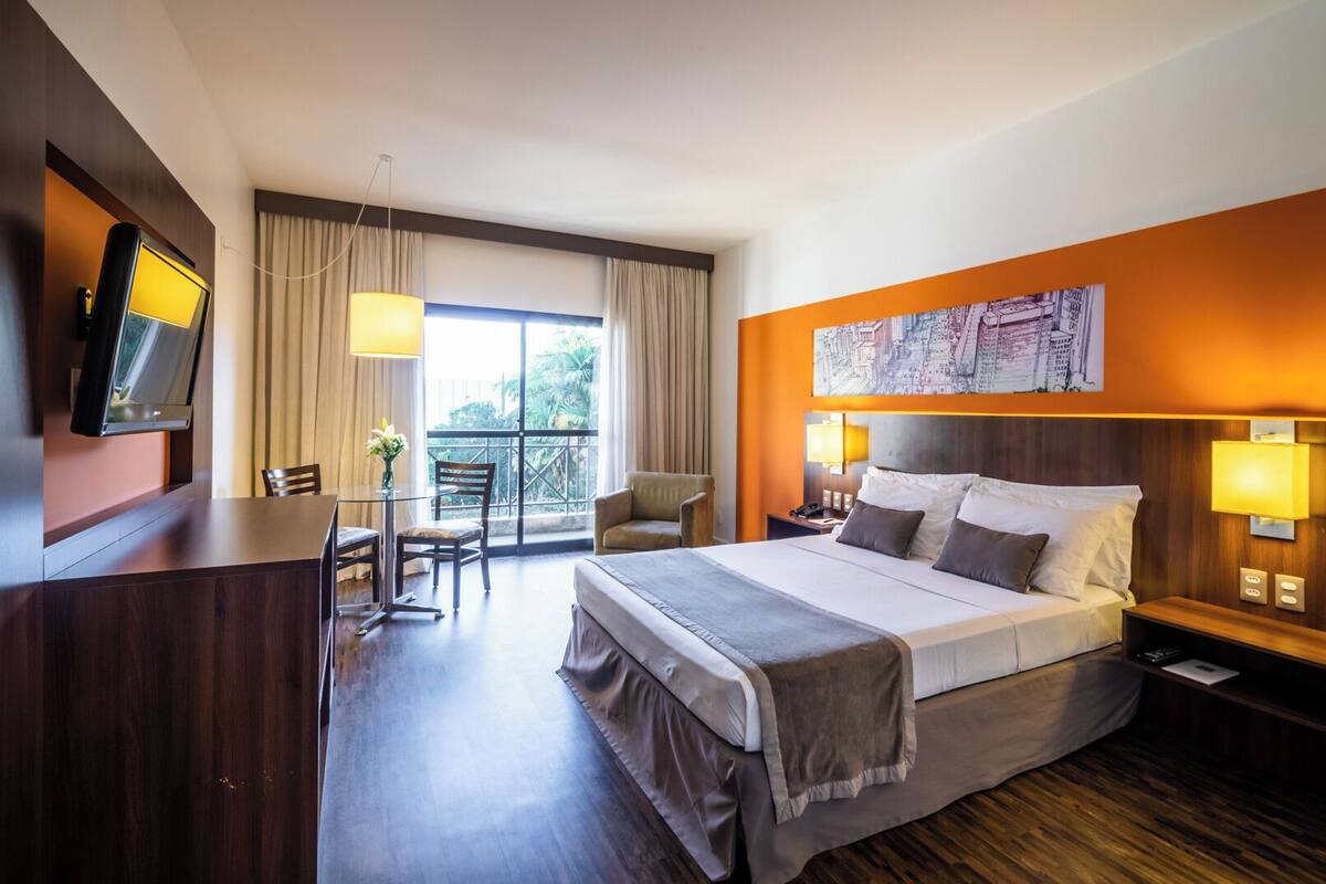 Une chambre d’hôtel avec un lit, un bureau, une chaise, une télévision et une fenêtre avec des rideaux.