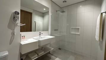A modern bathroom with a large mirror, two sinks, a shower, and a hairdryer.