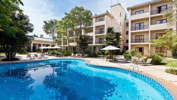 A swimming pool with lounge chairs and umbrellas, surrounded by a building with multiple balconies and windows.