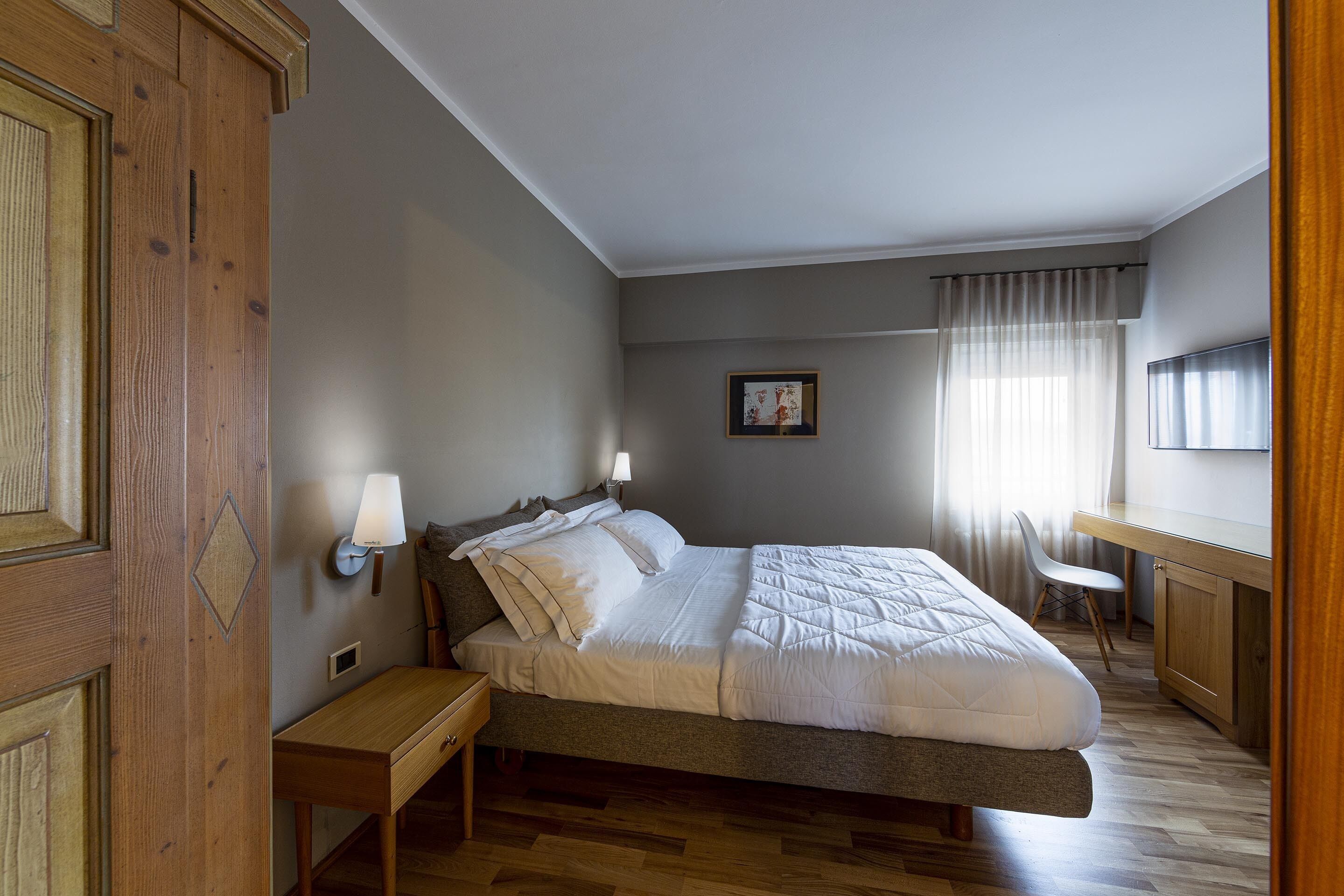 Une chambre à coucher comprenant un lit, des tables de chevet, un bureau, une chaise et un téléviseur.