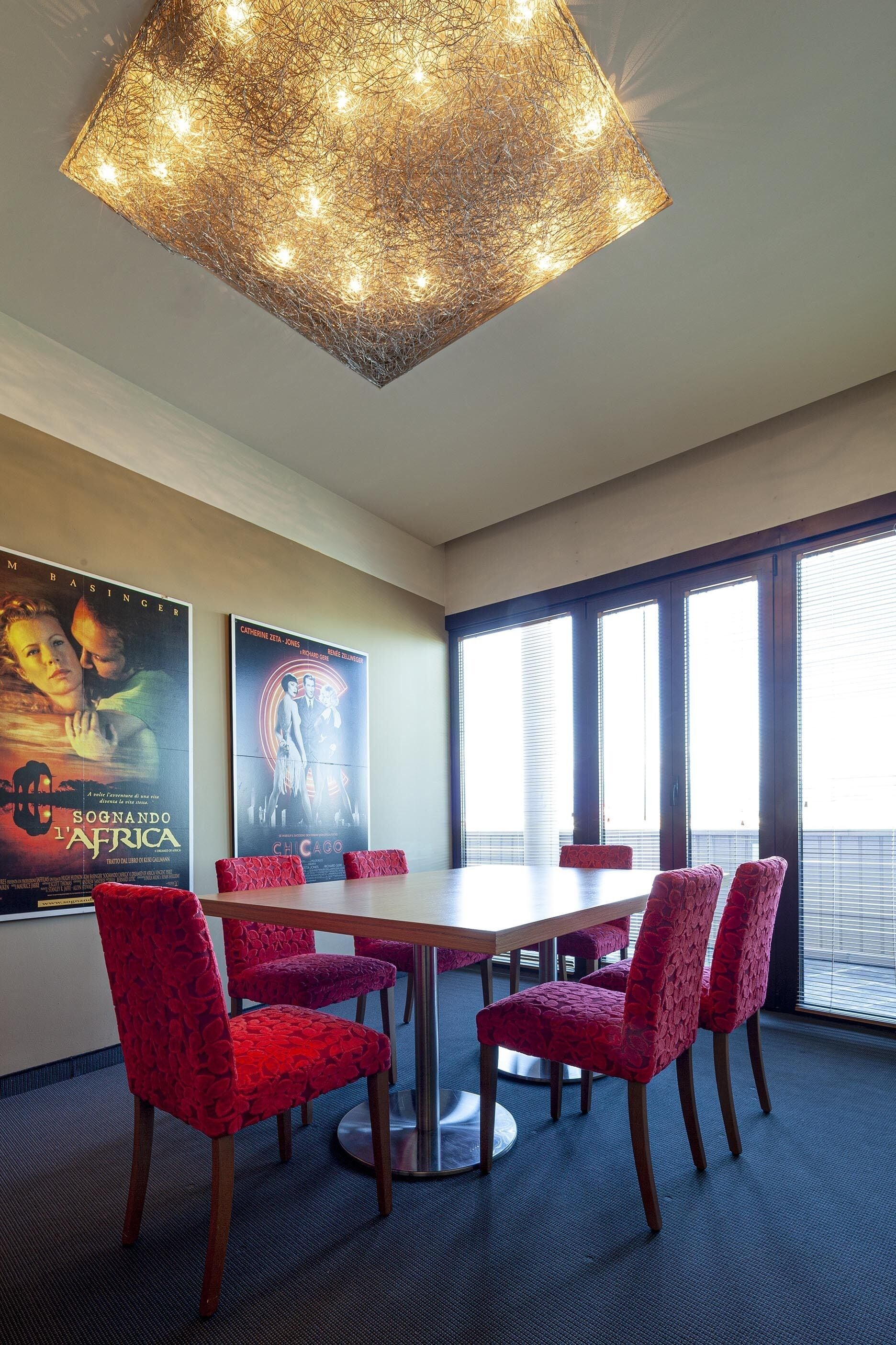 Una sala de conferències amb una taula gran i cadires tapissades de color vermell, cartells a la paret i una làmpada moderna.