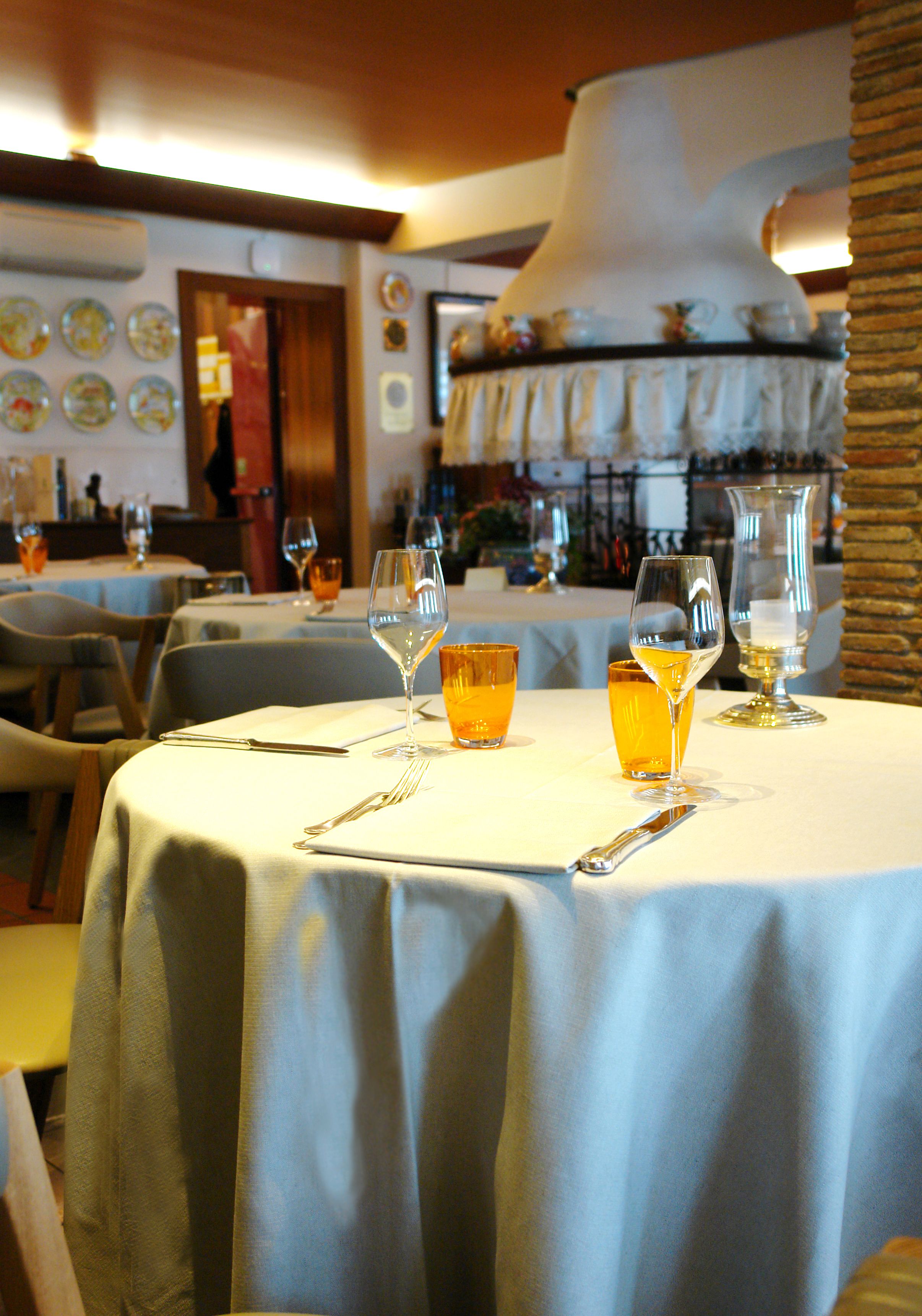 A restaurant interior with round tables, each set with wine glasses, cutlery, and a bottle.