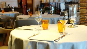 Interior de un restaurante con mesas redondas, cada una con copas de vino, cubiertos y una botella.