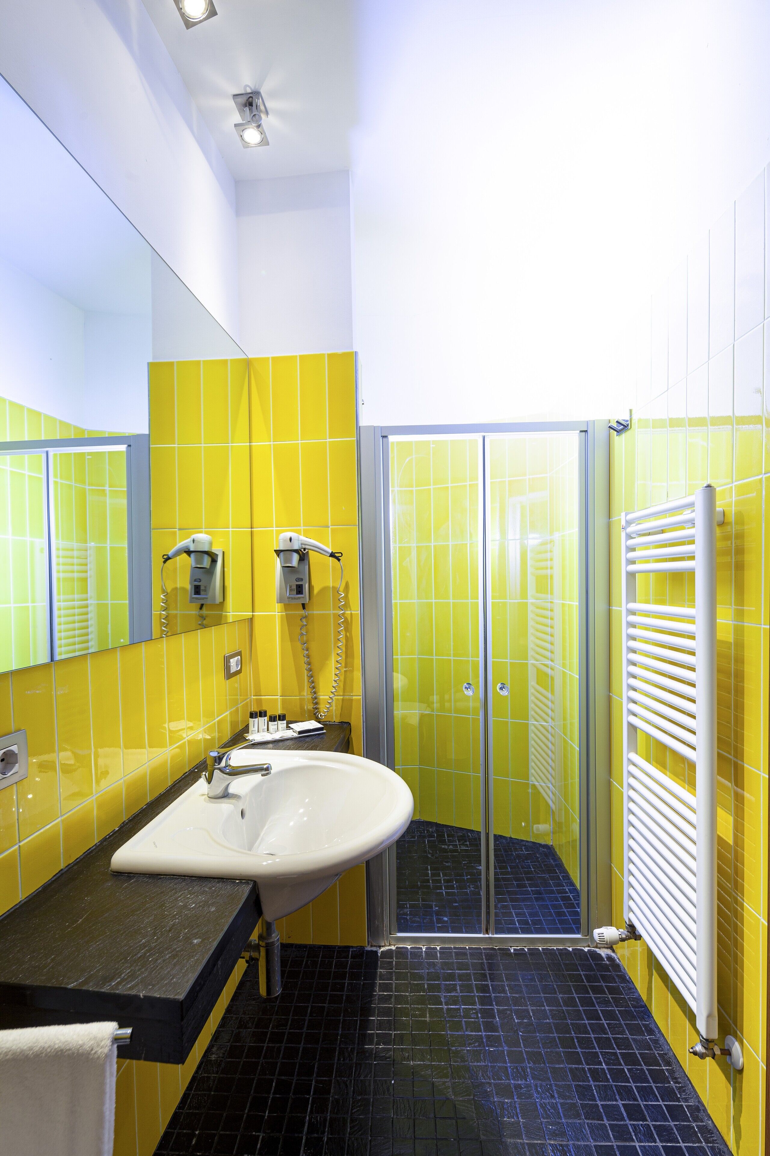 A bathroom with yellow walls, a black floor, a white sink, and a glass shower enclosure.