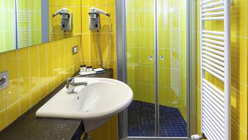 A bathroom with yellow walls, a black floor, a white sink, and a glass shower enclosure.