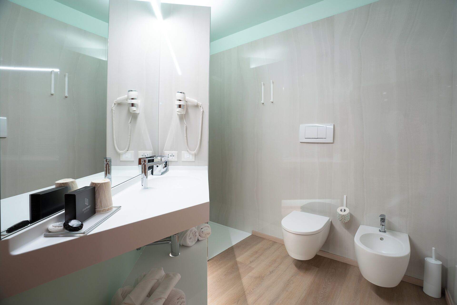 Un baño moderno con un espejo grande, un lavabo, un inodoro y un bidé.