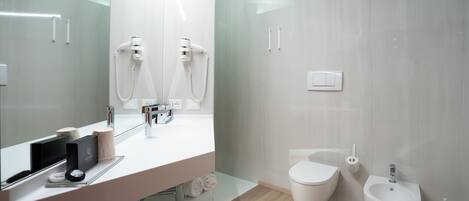 Un baño moderno con un espejo grande, un lavabo, un inodoro y un bidé.