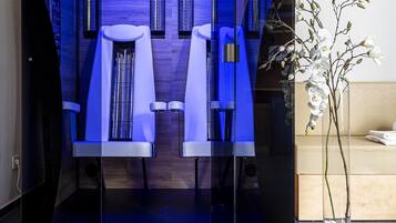 A modern spa room with a glass partition, two massage chairs, and a potted orchid.