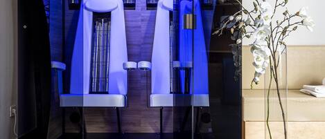A modern spa room with a glass partition, two massage chairs, and a potted orchid.