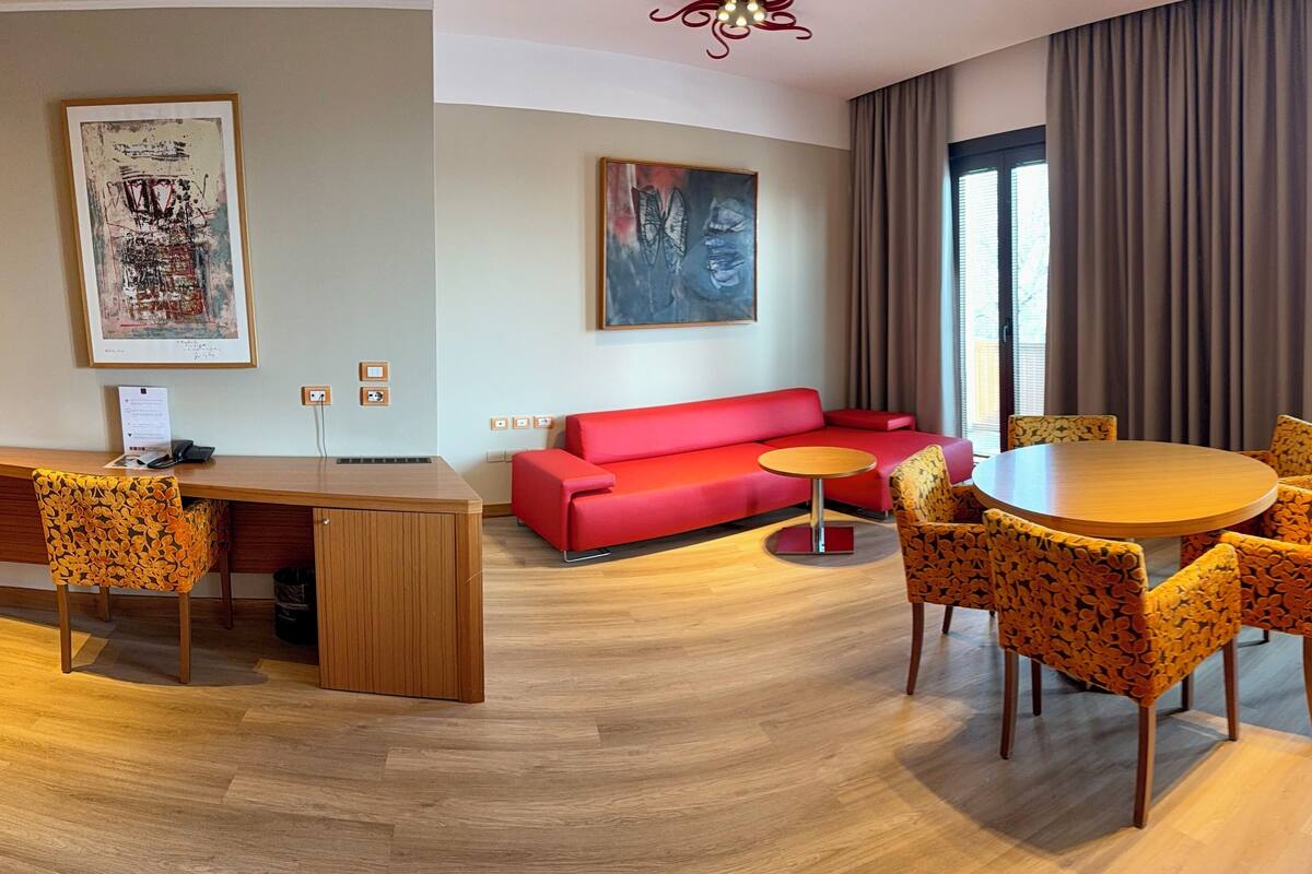Un salon moderne avec un canapé rouge, une table à manger en bois et des chaises à motifs, ainsi que des œuvres d’art accrochées aux murs.