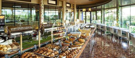 Un área de bufé con una variedad de pasteles y productos horneados, una estación de café y un espacio de estar con mesas y sillas.