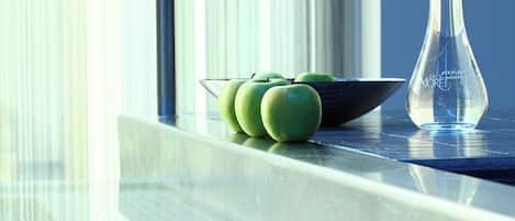 A modern kitchen with a glass-top table, a bowl of green apples, and a clear glass vase.